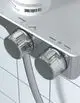 Thermostatsteuerung aus Chrom mit zwei Reglern zur Temperatureinstellung. Ideal Standard, montiert auf einer Ablage über weißen Fliesen.